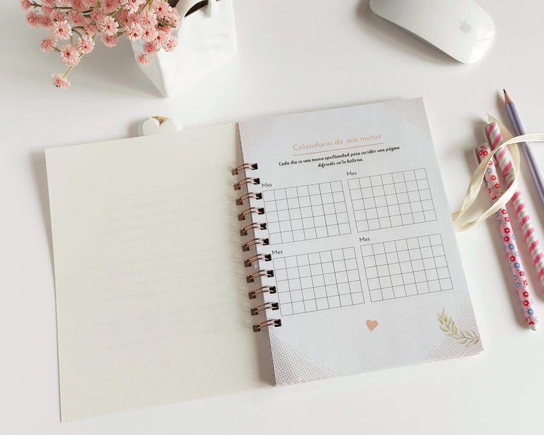 May include: A white and gold spiral bound notebook with a calendar grid on the right page. The calendar grid is labeled "Calendario de mis metas" and has a section for each month. The left page is blank.