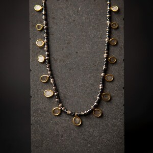 Op de afbeelding: Een zilveren en zwarte kralenketting met gouden accenten en heldere druppelvormige stenen die aan de ketting hangen.