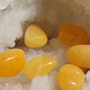 Peut inclure: Une collection de pierres lisses de couleur jaune-orange, de différentes tailles et formes, dans une grotte de cristal blanc.