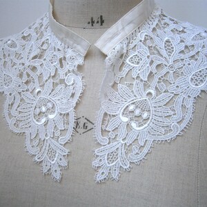 Puede incluir: Cuello de encaje blanco con dise&ntilde;o floral, expuesto sobre un maniqu&iacute;. El cuello presenta detalles intrincados y un delicado patr&oacute;n calado. Un accesorio de estilo vintage.
