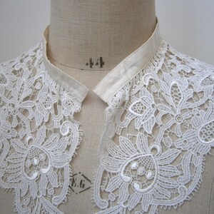 Puede incluir: Un cuello de encaje blanco con intrincados patrones florales y de hojas. El cuello se exhibe en un maniqu&iacute;, mostrando su delicado dise&ntilde;o y textura. Un accesorio de inspiraci&oacute;n vintage.