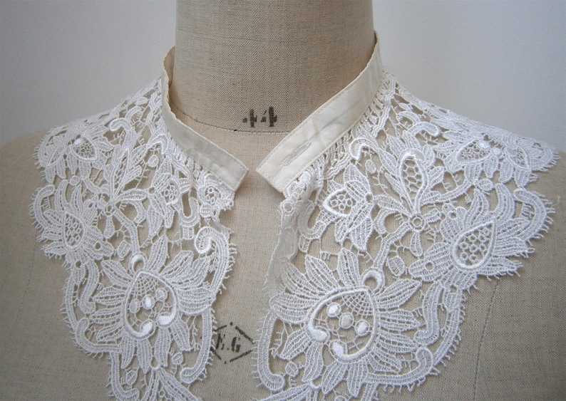 Puede incluir: Un cuello de encaje blanco con intrincados patrones florales y de hojas. El cuello se exhibe en un maniqu&iacute;, mostrando su delicado dise&ntilde;o y textura. Un accesorio de inspiraci&oacute;n vintage.