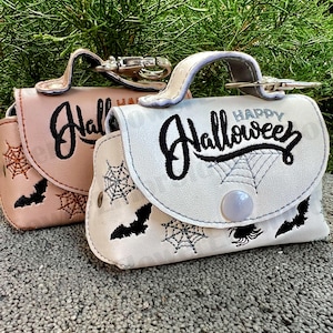 Könnte beinhalten: Zwei kleine Halloween-Taschen mit Stickereien. Eine ist weiß mit schwarzen Stickereien und sagt "Happy Hallowee", die andere ist rosa mit schwarzen Stickereien und sagt "Hall". Beide haben ein Spinnennetz- und Fledermausdesign.