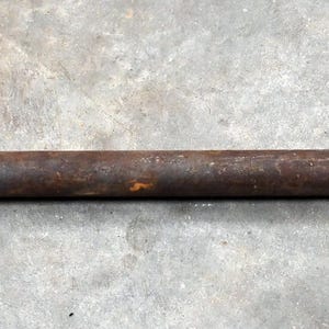 May include: A rusty, vintage pipe threading tool, featuring a circular die head and a long, cylindrical handle. The tool is made of metal and shows signs of age and use, with a weathered, brown patina. The tool is designed for cutting threads onto pipes.