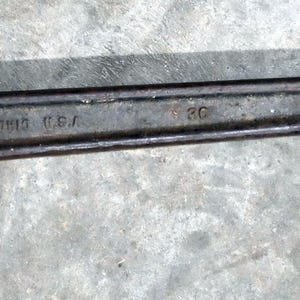 May include: A vintage, rusty pipe wrench with a long handle. The wrench is dark gray with areas of rust and the text "THE RIDGE TOOL CO. ELYRIA OHIO U.S.A." is visible. The adjustable jaw is open, ready for use. A classic tool for plumbing or mechanical work.