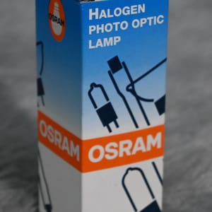 May include: A white box with orange and blue accents. The box contains a halogen photo optic lamp. The box has the text "OSRAM" printed on it.