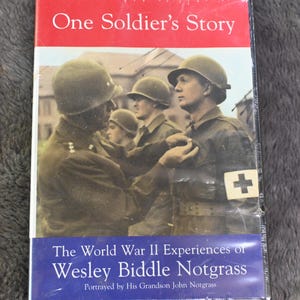 May include: A book titled "One Soldier's Story" with a red and blue cover. The cover features a black and white image of soldiers in uniform, with one receiving a medal. The text "The World War II Experiences of Wesley Biddle Notgrass" is also visible.