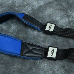 Peut inclure: Sangle de guitare bleue avec rembourrage noir et longueur réglable. La sangle porte l'inscription "Focal" aux deux extrémités.