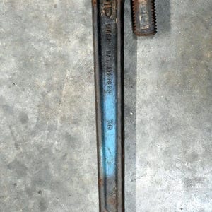 May include: A vintage pipe wrench with a rusty, textured head and a long, dark handle. The wrench has a blue stripe and the text "RIDGID" and "MADE IN U.S.A." is visible. A tool for plumbing and mechanical work.