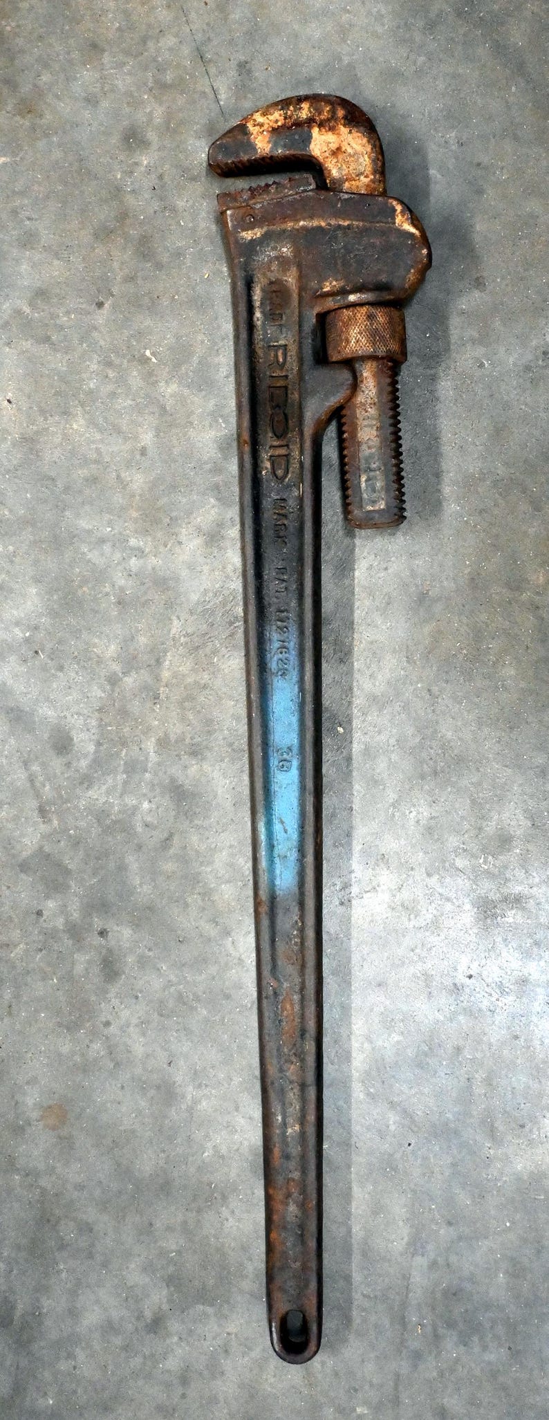 May include: A vintage pipe wrench with a rusty, textured head and a long, dark handle. The wrench has a blue stripe and the text "RIDGID" and "MADE IN U.S.A." is visible. A tool for plumbing and mechanical work.