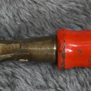 May include: A well-used chisel with a metal blade and a clear plastic handle. The handle has a red band near the blade. The metal blade shows signs of wear and tear, indicating frequent use. The tool is designed for woodworking or similar tasks.