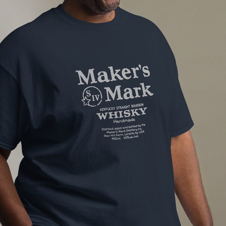 May include: A navy blue t-shirt with a white graphic of a Maker's Mark whiskey label. The label reads "Maker's Mark Kentucky Straight Bourbon Whiskey Handmade Distilled, aged and bottled by the Maker's Mark Distillery, Inc. Star Hill Farm, Loretta, Ky USA 750ml 45% alc/vol."