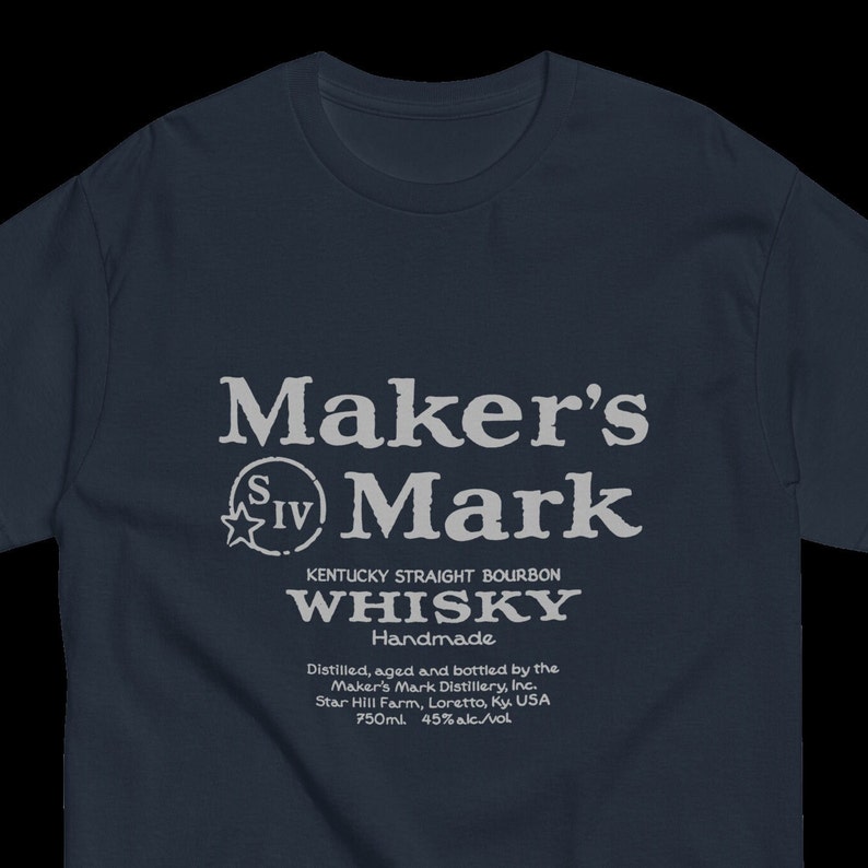 May include: A navy blue t-shirt with a white graphic of the Maker's Mark whiskey label. The label features the brand name, a star with the Roman numeral IV, and the text "Kentucky Straight Bourbon Whiskey Handmade". The label also includes the distillery's name, location, and bottle size.
