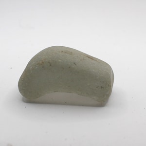 May include: A smooth, light green sea glass stone with a rounded shape.