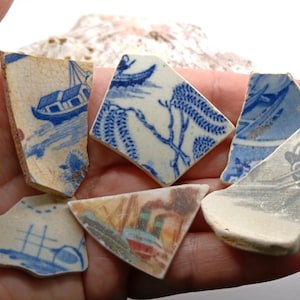 May include: Six pieces of blue and white porcelain pottery with various designs, including a boat, flowers, and a bird. The pieces are broken and have a white background with blue paint.
