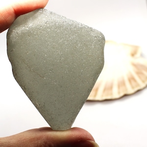 Puede incluir: Una pieza de vidrio de mar gris claro con forma de diamante y una superficie lisa y esmerilada.