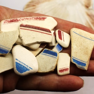 May include: A collection of white ceramic sea glass with blue and red stripes. The sea glass is smooth and worn from being in the ocean.