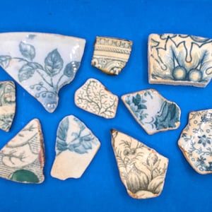 以下が含まれることがあります： 青と白の花柄と植物柄が施された、アンティークの陶器の破片のコレクション。さまざまなサイズと形状の破片は、青色の背景に複雑なデザインを示しています。