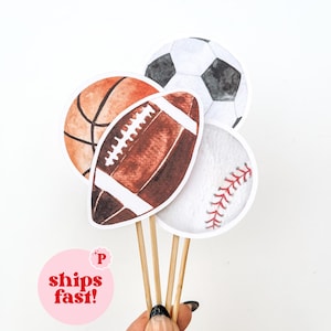 May include: Watercolor sports-themed cupcake toppers. The toppers include a basketball, football, soccer ball, and baseball. The text "ships fast!" is in a pink circle.