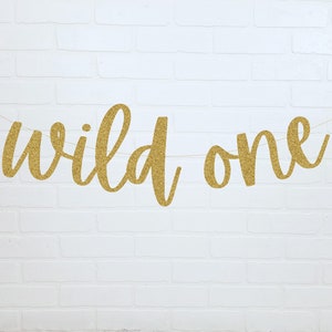 May include: Gold glitter banner with the text "wild one" in a cursive font.