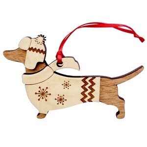 K&ouml;nnte beinhalten: Weihnachtsbaumschmuck aus Holz in Form eines Dackels, der eine gestrickte M&uuml;tze und einen Schal mit Schneeflockenmuster tr&auml;gt. Der Anh&auml;nger hat ein rotes Band zum Aufh&auml;ngen.
