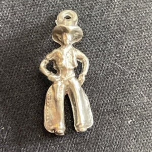 May include: Silver charm of a cowboy wearing a hat and chaps.