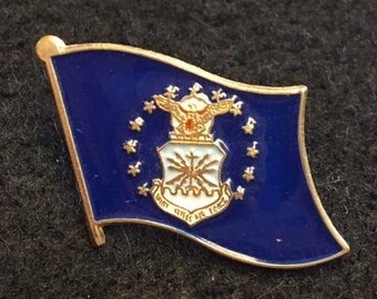 Op de afbeelding: Een blauwe en gouden emaille pin met het embleem van de United States Air Force met de woorden "United States Air Force" rond het embleem.