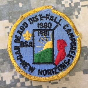 May include: A blue and yellow embroidered patch with the text "New Horizons District E-Fall 1980 Camp Horseshoe BSA" and a graphic of a sunrise over a green hill.