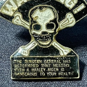 May include: A black and gold warning sign with a skull and crossbones. The text reads "WARNING! THE SURDEEN GENERAL HAS DETERMINED THAT MESSING WITH A HARLEY RIDER IS DANGEROUS TO YOUR HEALTH."