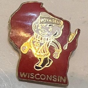 May include: A vintage pin in the shape of Wisconsin, featuring a cartoon character labeled "Voyageur." The pin is red with gold trim and text, including "Wisconsin" at the bottom and "40" on the character's outfit. The character is wearing a hat and scarf.