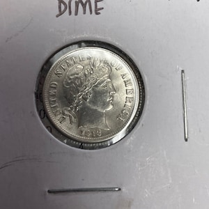 May include: A silver Barber Dime coin with the inscription "United States of America" and the date "1918".