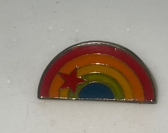 Op de afbeelding: Een regenboogkleurige emaille pin met een rode ster in het midden. De pin heeft de vorm van een halve cirkel.