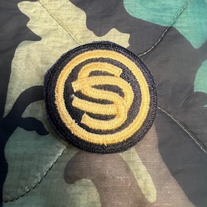 May include: A black and gold embroidered patch with the letter "S" in a circle.