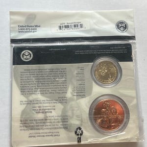 K&ouml;nnte beinhalten: Versiegelte Verpackung der United States Mint mit einer goldfarbenen M&uuml;nze und einer Bronzemedaille. Die Verpackung enth&auml;lt Text und einen Barcode. Die M&uuml;nzen sind f&uuml;r Ronald Reagan.