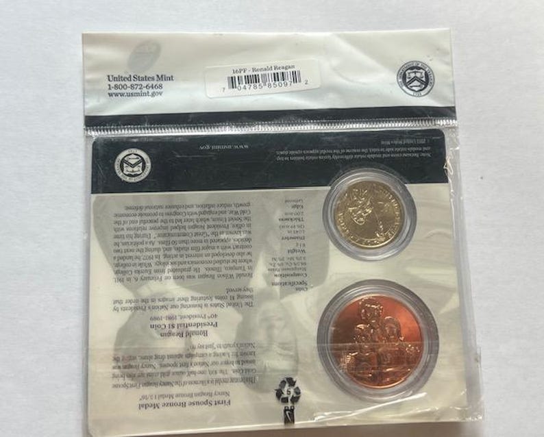 K&ouml;nnte beinhalten: Versiegelte Verpackung der United States Mint mit einer goldfarbenen M&uuml;nze und einer Bronzemedaille. Die Verpackung enth&auml;lt Text und einen Barcode. Die M&uuml;nzen sind f&uuml;r Ronald Reagan.