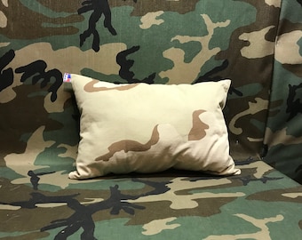 Op de afbeelding: Een beige kussen met een camouflagepatroon op een camouflage achtergrond.