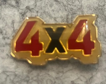 Op de afbeelding: Een goudkleurige metalen pin met de tekst "4X4" in rood en zwart. De pin heeft een rechthoekige vorm met afgeronde randen. De cijfers "4" zijn rood en de "X" is zwart.