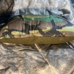 May include: A camouflage-patterned pillow with a quilted design and a brown felt backing.