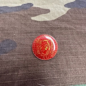 May include: A red and gold enamel pin with a cartoon cat face design.