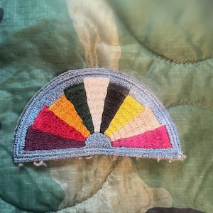 May include: A blue and white embroidered patch with a rainbow design. The patch is shaped like a half circle and has a frayed edge.