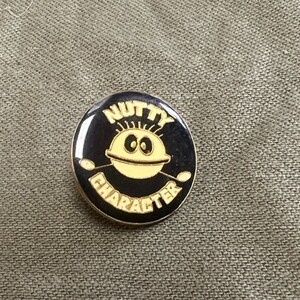 May include: A black and gold pin with a cartoon face and the words "Nutty Character" around the edge.