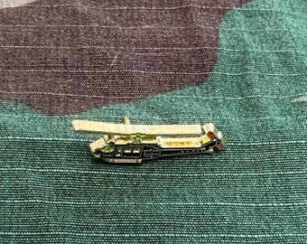 Op de afbeelding: Een gouden pin van een zwarte helikopter met rode en witte accenten. De helikopter vliegt met draaiende rotorbladen.