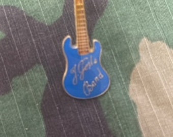 Op de afbeelding: Een blauwe en gouden gitaarpin met de tekst "J. Girls Band" erop.