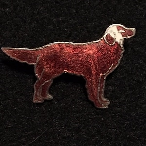 May include: A red enamel dog pin with white accents. The dog is standing in profile and has a long tail.