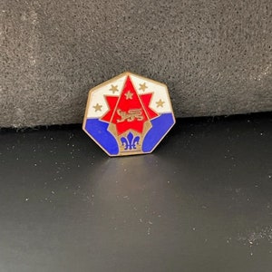 May include: A gold-colored pin with a red star and blue and white accents. The pin features a stylized lion and the text "1955".