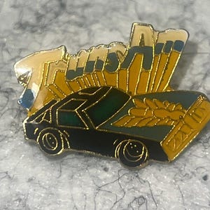 May include: A vintage pin featuring a black car with gold accents and the word "Tulsa" in gold and blue. The pin has a detailed design with a classic car and a decorative element.