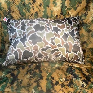 May include: A camouflage-patterned pillow with a white background and brown, green, and black accents.