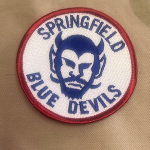 May include: A red, white, and blue embroidered patch with the text "Springfield Blue Devils" and a blue devil mascot with horns.