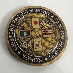 May include: A gold-colored coin with a world map design and the text "WESTERN PACIFIC JAPAN CENTRAL PACIFIC KOREA" around the edge. The map features flags of Japan, Korea, the Philippines, and Hawaii.