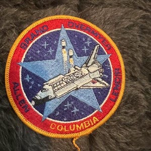 May include: A red, white, and blue embroidered patch with a space shuttle, stars, and the text "BRAND OVERMYER ALLEN COLUMBIA LEMON".